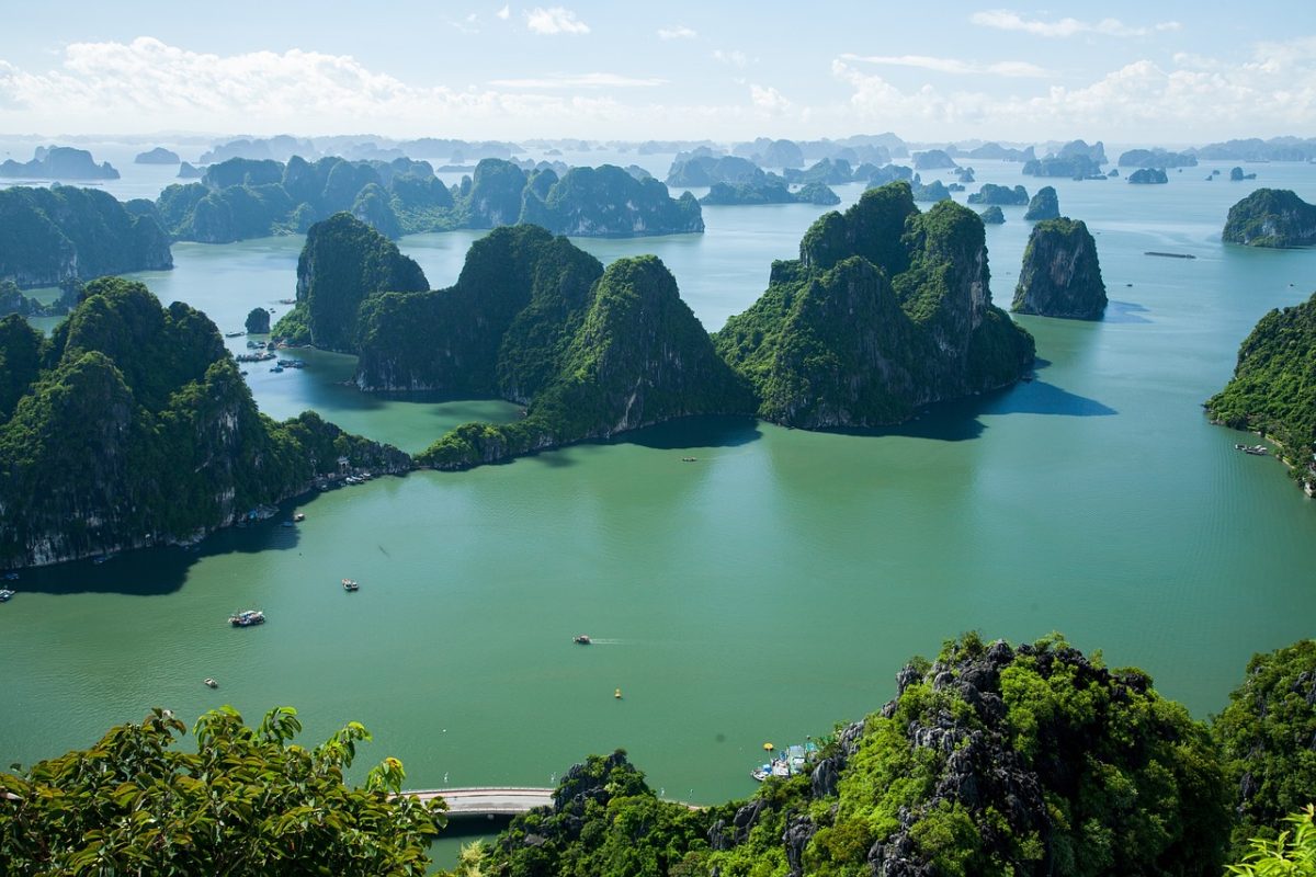 A stunning aerial view of Halong Bay, featuring its iconic limestone islands rising from turquoise waters, dotted with small floating villages and lush greenery
