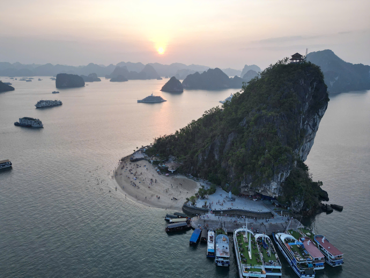 Titop Island beach and viewpoint during a Halong Bay day trip, with cruise boats and a sunset backdrop