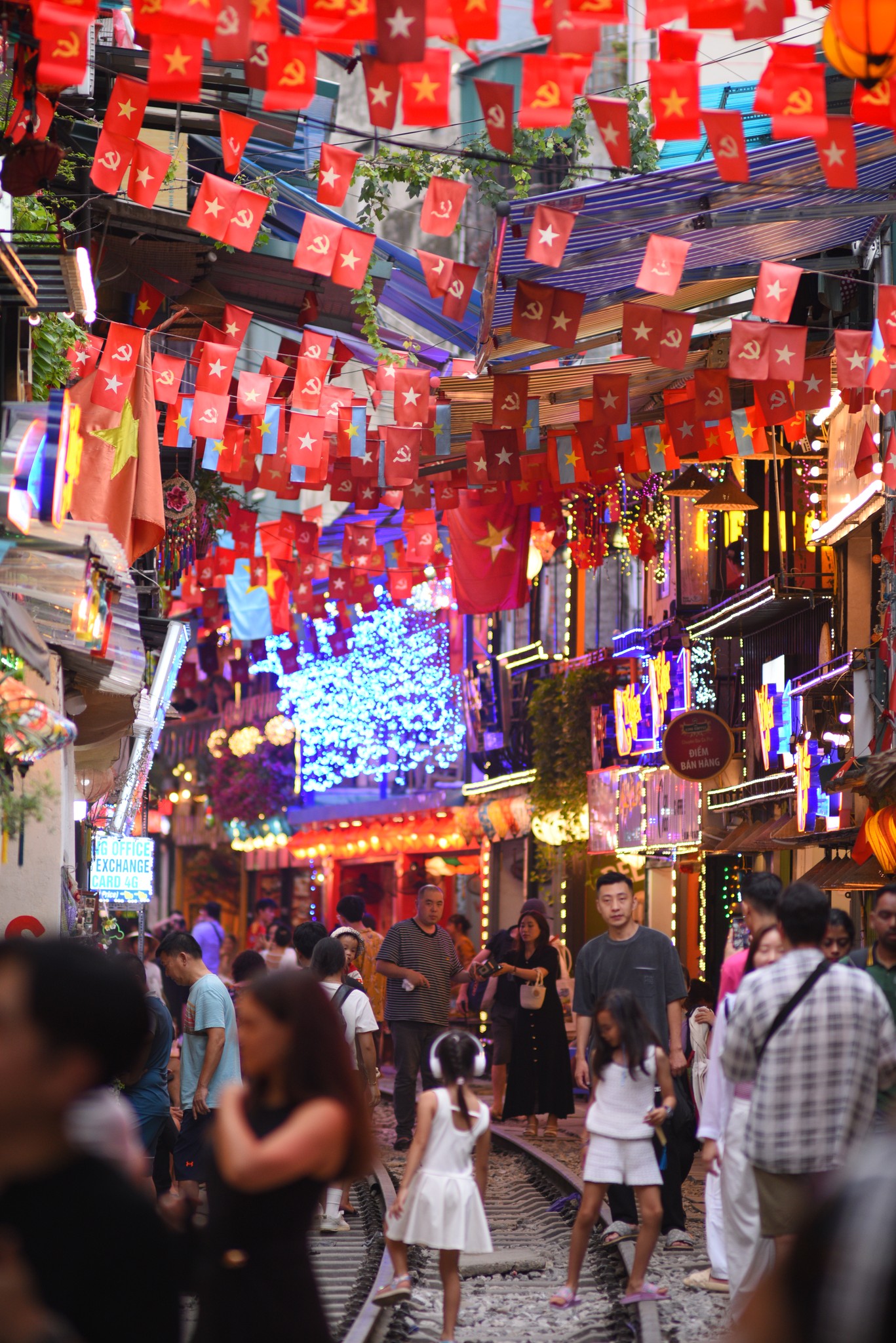 Tourists and children enjoying the vibrant night atmosphere of Hanoi Train Street, beautifully decorated with red flags and yellow stars to celebrate Vietnam National Day 80 Years
